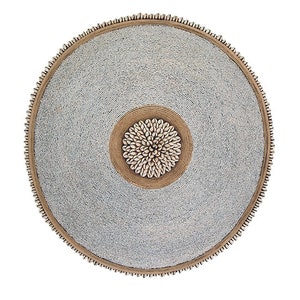 Op de afbeelding: Een ronde, geperde wanddecoratie met een centraal ontwerp van witte schelpen in een bruine cirkel. De kralen zijn wit en de buitenrand is bruin.