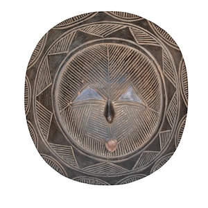 Op de afbeelding: Een rond, donkerbruin houten masker met een gesneden gezicht en geometrische patronen. Het masker heeft een gesneden neus, ogen en mond.