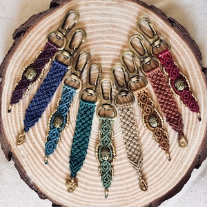 Può includere: Un set di dieci portachiavi in macramè colorati con un ciondolo a forma di Buddha in ottone. Ogni portachiavi presenta un colore e uno schema di macramè diversi.