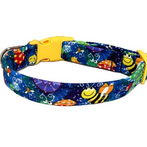 May include: A blue pet collar featuring a repeating pattern of cartoon bees, ladybugs, and purple snail shells on a dark blue background with white stars. The collar includes a bright yellow plastic side-release buckle and a metal D-ring.