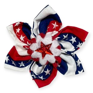 May include: A red, white, and blue fabric flower with a red star in the center. The flower is made of a patterned fabric with white stars on a blue background.