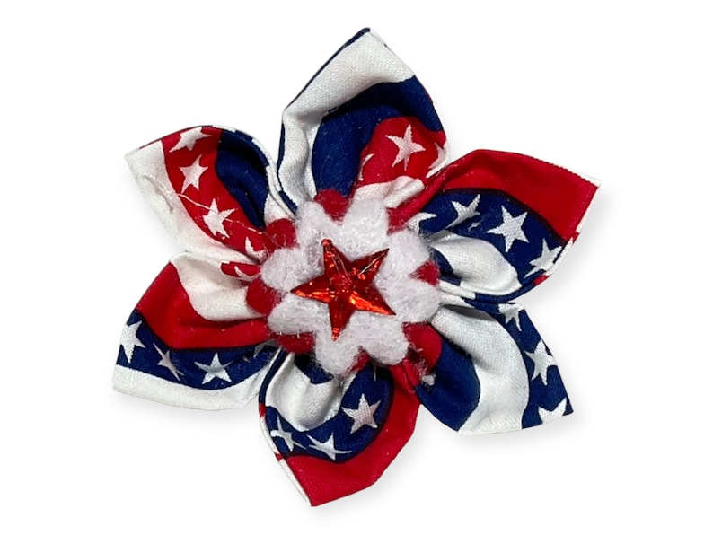 May include: A red, white, and blue fabric flower with a red star in the center. The flower is made of a patterned fabric with white stars on a blue background.
