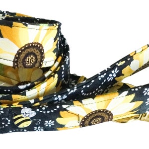 May include: A black and yellow dog leash with a sunflower and bee pattern. The leash has a gold metal clip.