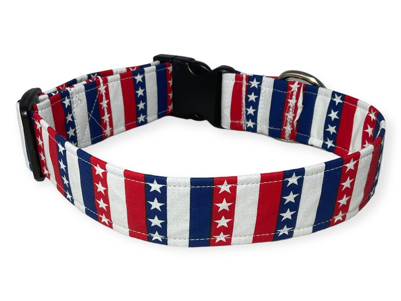 May include: A red, white, and blue dog collar with a stars and stripes pattern. The collar has a black plastic buckle and a silver metal D-ring.