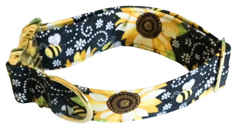 May include: A black dog collar with a sunflower and bee pattern. The collar is made of fabric and has a gold metal buckle and D-ring.