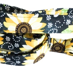 May include: A black dog leash with a sunflower and bee pattern. The leash has a gold metal clip.