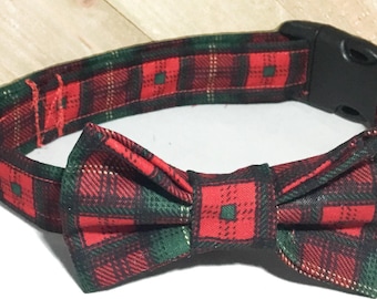 May include: A pet collar featuring a red and dark green plaid pattern with a matching fabric bow tie attached to the front. The collar includes a black plastic side-release buckle, a black plastic adjustable slider, and a silver metal D-ring.