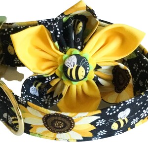 May include: A black dog collar with a sunflower and bee pattern. A yellow flower with a bee button is attached to the collar.