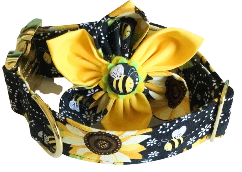 May include: A black dog collar with a sunflower and bee pattern. A yellow flower with a bee button is attached to the collar.