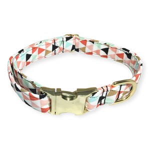 May include: A colorful dog collar with a geometric pattern in shades of pink, blue, and black. The collar has a gold metal buckle and a D-ring.