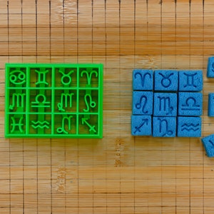 May include: A set of green and blue zodiac sign stamps. The green stamps are arranged in a grid, while the blue stamps are scattered around. The stamps are made of plastic and have a raised design.