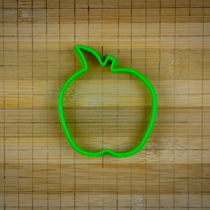 Peut inclure: Un emporte-pi&egrave;ce en forme de pomme en plastique vert sur une planche &agrave; d&eacute;couper en bambou.