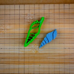 Puede incluir: Dos cortadores de galletas con forma de concha, uno verde y otro azul, sobre una tabla de cortar de bambú.