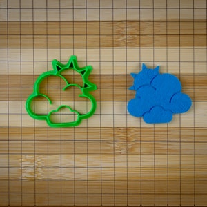 Może przedstawiać: Dwa wykrawacze do ciasteczek, jeden zielony, a drugi niebieski, w kształcie chmur z słońcem i gwiazdą na górze.