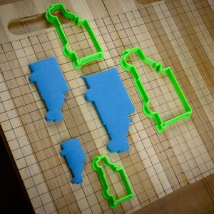 May include: A set of cookie cutters in the shape of trucks. The cutters are made of green plastic and are arranged on a wooden chopping board.