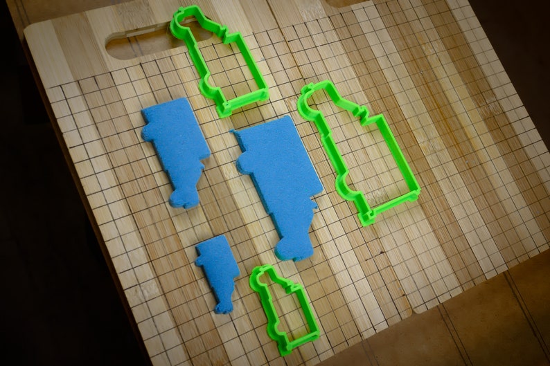 May include: A set of cookie cutters in the shape of trucks. The cutters are made of green plastic and are arranged on a wooden chopping board.