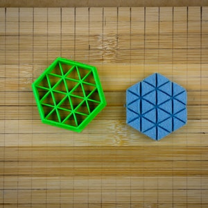 Può includere: Due tagliabiscotti esagonali, uno verde e uno blu, su un tagliere di legno. Entrambi i tagliabiscotti hanno un design geometrico.