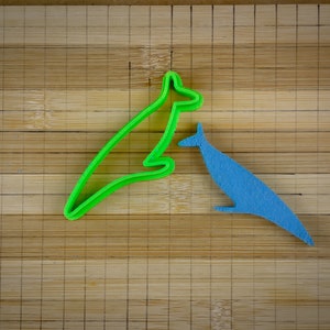 May include: Two kangaroo cookie cutters, one green and one blue, on a wooden surface.