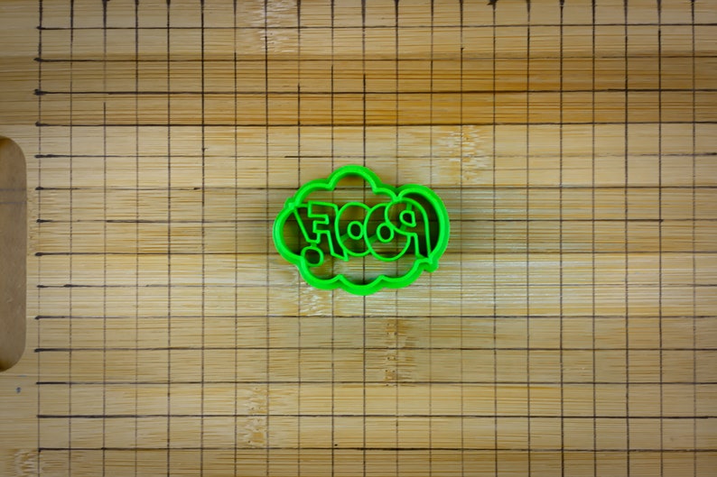 May include: Green plastic cookie cutter shaped like a speech bubble with the word "POOF" inside.