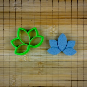 Può includere: Due stampini per biscotti a forma di fiore di loto, uno verde e uno blu, su un tagliere di bambù.