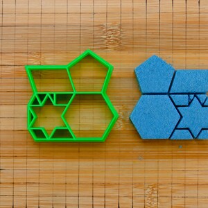 May include: Two cookie cutters, one green and one blue, shaped like a honeycomb with a star in the center.