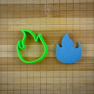 May include: Two flame-shaped cookie cutters, one green and one blue, on a wooden surface.