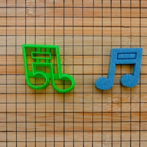 May include: Two plastic cookie cutters shaped like musical notes. The note on the left is green and the note on the right is blue.