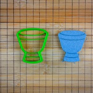 Op de afbeelding: Een groene plastic koekjesvormpje en een blauwe suikerkoek, beide in de vorm van een trommel.