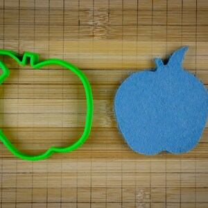 Peut inclure: Un emporte-pi&egrave;ce en forme de pomme en plastique vert &agrave; c&ocirc;t&eacute; d'une pomme en feutre bleu.