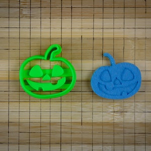 Op de afbeelding: Twee Halloween-thema koekjesvormen, een groene en een blauwe, in de vorm van pompoenen met uitgesneden gezichten.