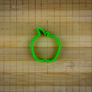 Peut inclure: Un emporte-pi&egrave;ce en forme de pomme en plastique vert sur une surface en bois.