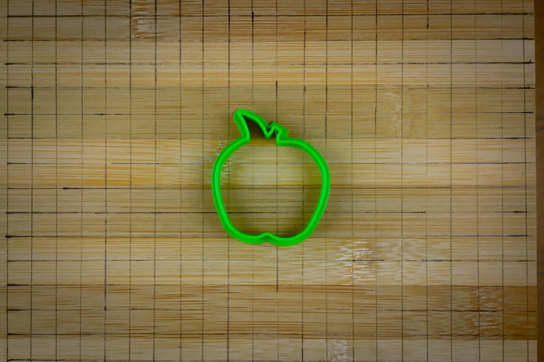 Peut inclure: Un emporte-pi&egrave;ce en forme de pomme en plastique vert sur une surface en bois.