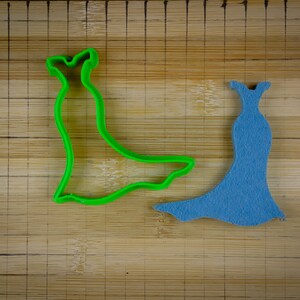 May include: Two dress-shaped cookie cutters, one green and one blue, on a wooden cutting board.
