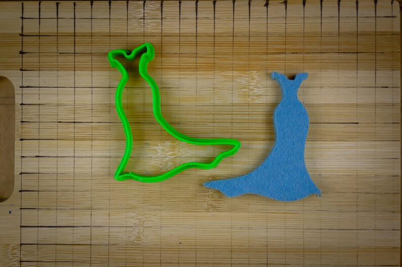 May include: Two dress-shaped cookie cutters, one green and one blue, on a wooden cutting board.