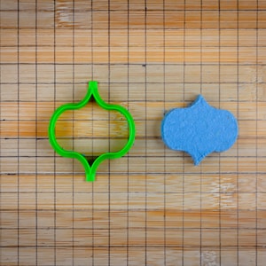 May include: A green plastic cookie cutter shaped like a quatrefoil, and a blue fondant cookie in the same shape.