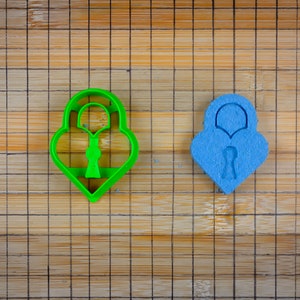May include: Two lock-shaped cookie cutters, one green and one blue, on a bamboo chopping board.