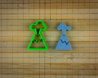 May include: Two volcano cookie cutters, one green and one blue, on a bamboo chopping board.