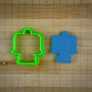 May include: A green plastic cookie cutter and a blue sugar cookie, both shaped like a cake with candles.