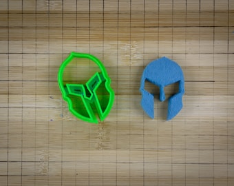 Könnte beinhalten: Zwei spartanische Helm-Ausstecher, einer grün und einer blau, auf einer Holzoberfläche.