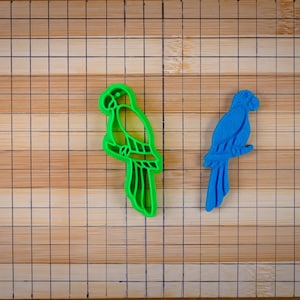 Può includere: Due stampini per biscotti in plastica a forma di pappagalli. Il pappagallo a sinistra è verde e il pappagallo a destra è blu.