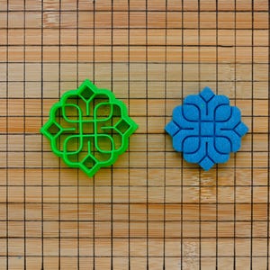 Könnte beinhalten: Zwei Ausstecher, einer grün und einer blau, mit einem geometrischen Design. Die Ausstecher befinden sich auf einer Holzoberfläche.