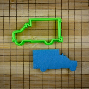 May include: A green plastic cookie cutter shaped like a delivery van, and a blue cookie cutter shaped like a delivery van on a bamboo chopping board.