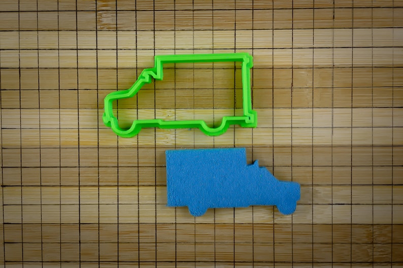 May include: A green plastic cookie cutter shaped like a delivery van, and a blue cookie cutter shaped like a delivery van on a bamboo chopping board.