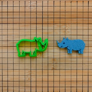 May include: Two rhino cookie cutters, one green and one blue, on a wooden cutting board.