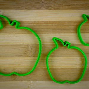 Peut inclure: Trois emportes-pi&egrave;ces en forme de pomme en plastique vert de diff&eacute;rentes tailles sur une surface en bois.