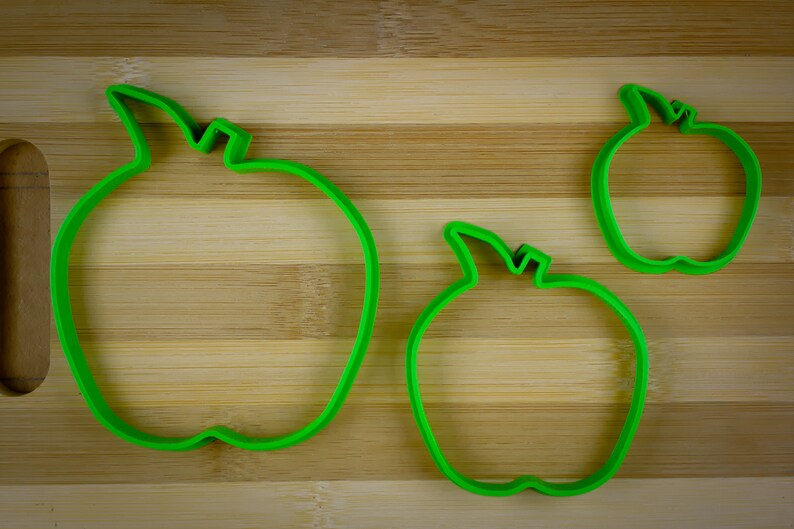 Peut inclure: Trois emportes-pi&egrave;ces en forme de pomme en plastique vert de diff&eacute;rentes tailles sur une surface en bois.