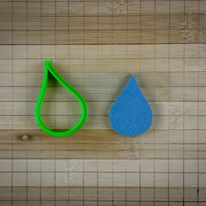 May include: A green plastic cookie cutter shaped like a water drop next to a blue felt water drop.
