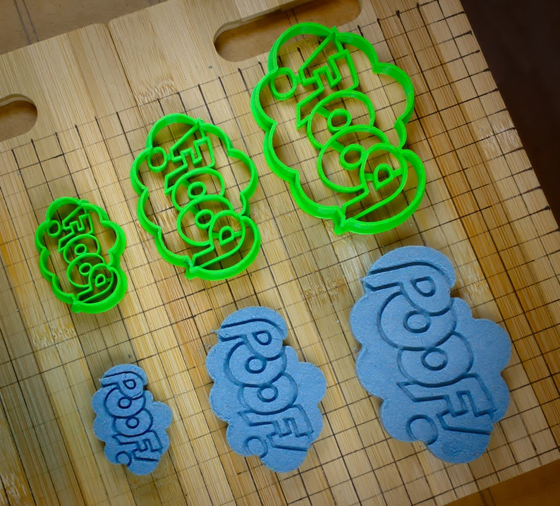 May include: Five cookie cutters on a wooden surface. The cookie cutters are green and blue and shaped like clouds with words on them. The words on the cookie cutters are "Foodie", "Foodie", "Foodie", "Roodie", and "Roodie".