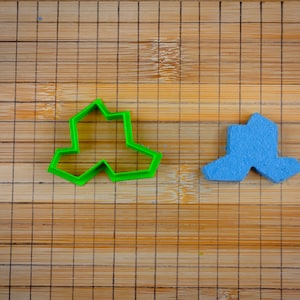 Könnte beinhalten: Zwei Ausstecher auf einem Bambus-Schneidebrett. Der Ausstecher links ist grün und hat die Form eines dreispitzigen Sterns. Der Ausstecher rechts ist blau und hat die Form eines dreispitzigen Sterns.