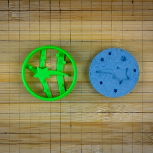 Peut inclure: Deux emportes-pièces, l'un vert et l'autre bleu, en forme d'étoile filante avec une étoile à l'extrémité. L'emporte-pièce vert présente un motif en relief de lignes autour de l'étoile.